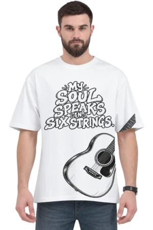 Male model wearing a white oversized T-shirt featuring “My Soul Speaks in Six Strings” typography and a black-and-white acoustic guitar graphic, paired with dark jeans and a black watch.