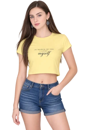 Female fashion model wearing a pale yellow cropped T-shirt with the quote “In Search of You, I Found Myself” paired with denim shorts.