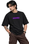 Clean-shaven male model wearing an oversized black T-shirt with bold purple “UNCHAINED” lettering