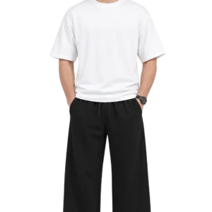 Indian male model wearing relaxed black wide-leg pants with an elastic drawstring waist, paired with a white oversized T-shirt and white sneakers.