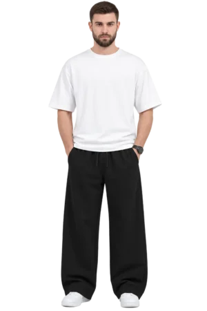 Indian male model wearing relaxed black wide-leg pants with an elastic drawstring waist, paired with a white oversized T-shirt and white sneakers.