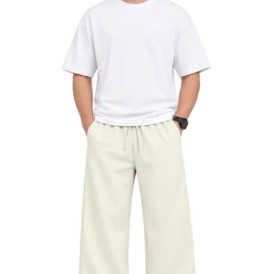 Male model wearing cream-colored wide-leg relaxed fit pants with an elastic drawstring waist, styled with a white oversized T-shirt and white sneakers.