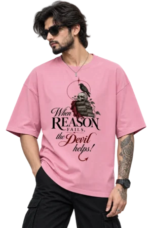 Male fashion model wearing a dusty pink oversized T-shirt featuring a gothic skull, raven, books and the quote “When Reason Fails, the Devil helps!